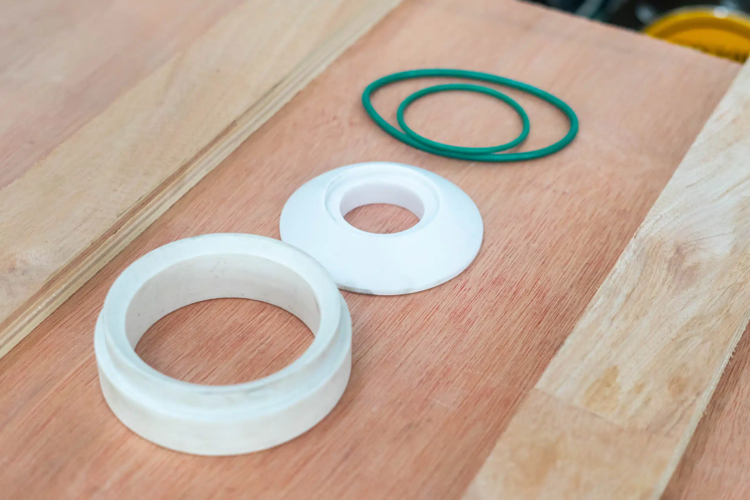 Ceramic valve seat and liner parts with O-rings on a wooden surface.