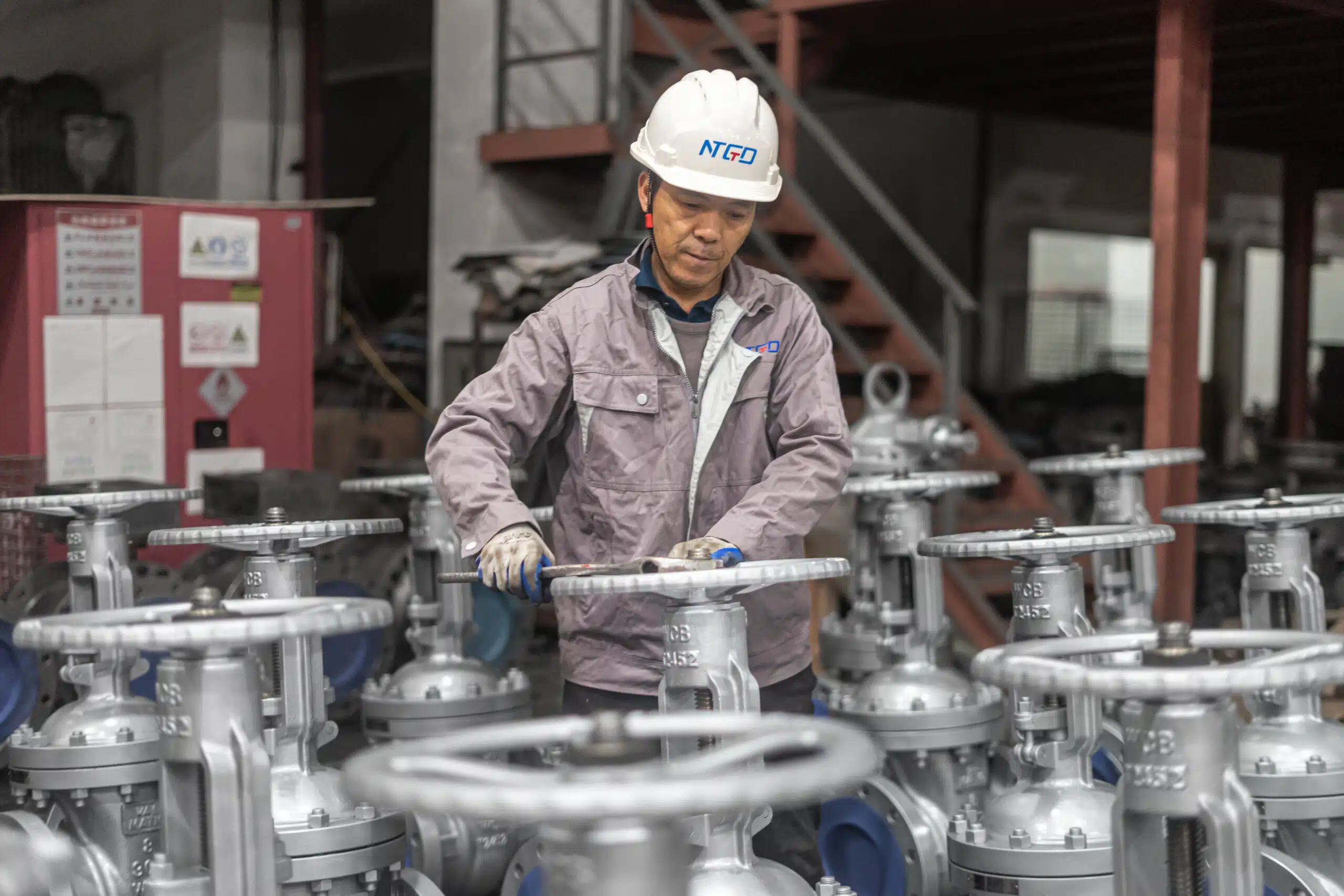 Worker inspecting multiple flanged gate valves with handwheels in the NTGD workshop