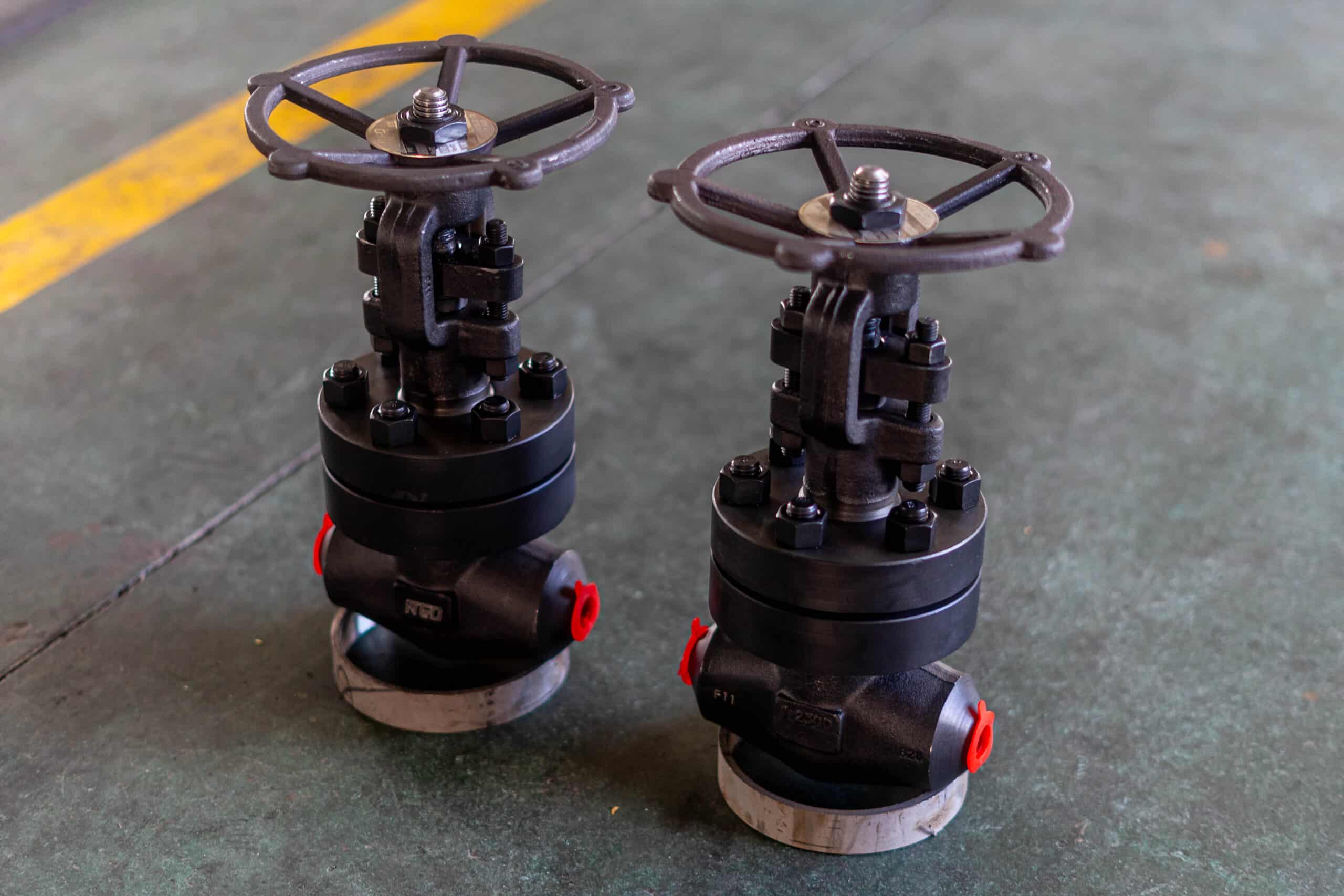Forged steel globe valves with handwheels and bolted bonnets on a workshop floor.