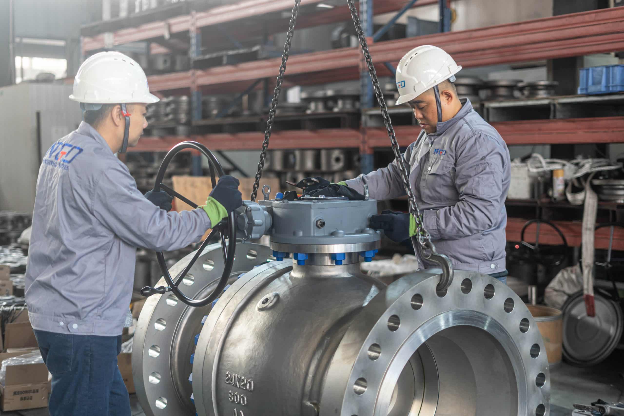 Workers assembling a large flanged ball valve in a real factory workshop