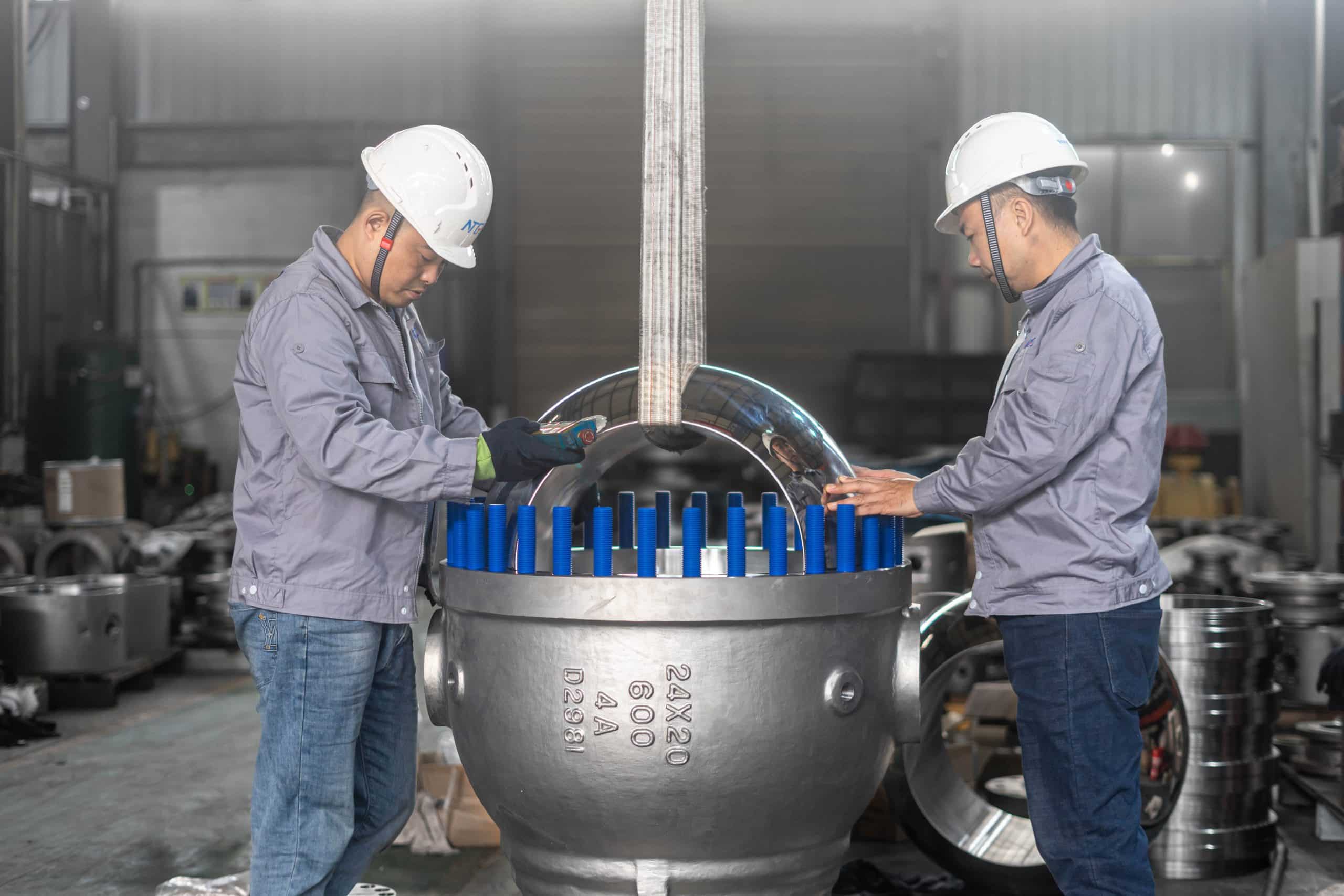 Workers inspecting a large trunnion ball valve body and seat area in the workshop