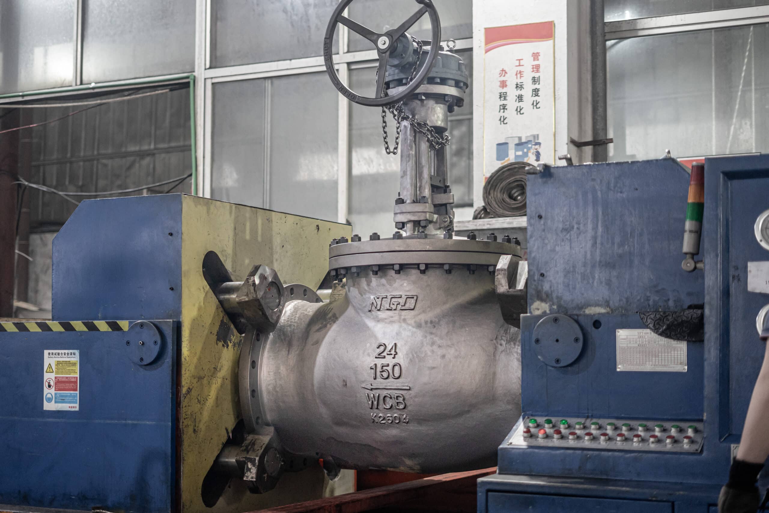 Large industrial globe valve undergoing pressure testing in a workshop with visible body marking.