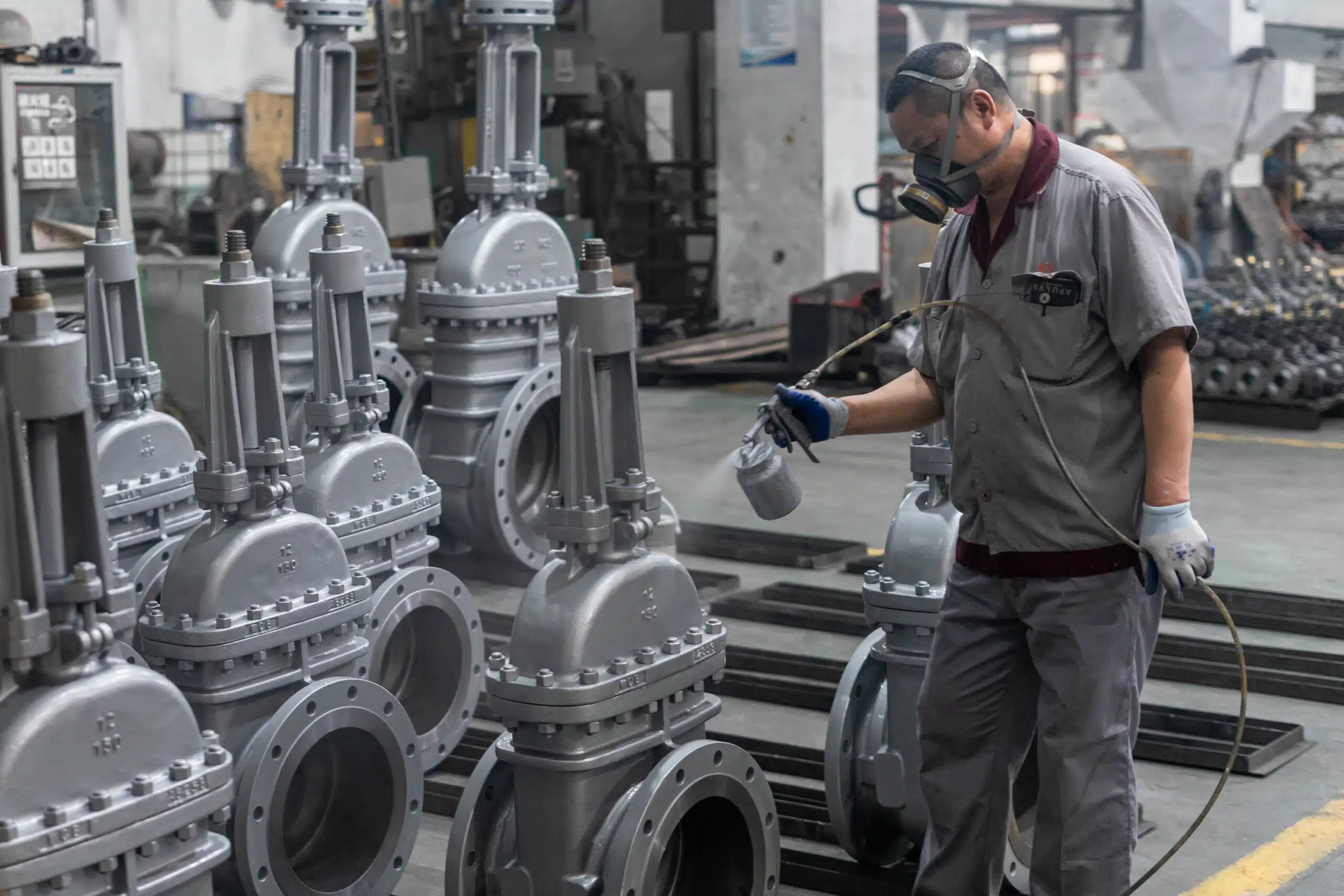 Travailleur appliquant un revêtement protecteur sur des vannes industrielles pour les protéger contre la corrosion